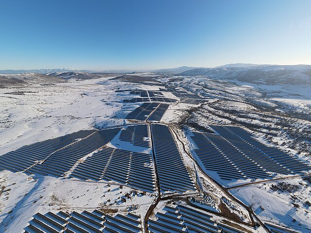 The Kozani solar park from a bird's-eye view in winter, with snow covering the landscape and the sky being bright blue.